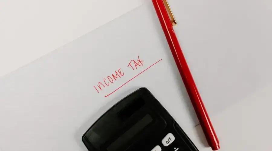 Close-up of a calculator and red pen on paper labeled 'Income Tax', representing financial planning.