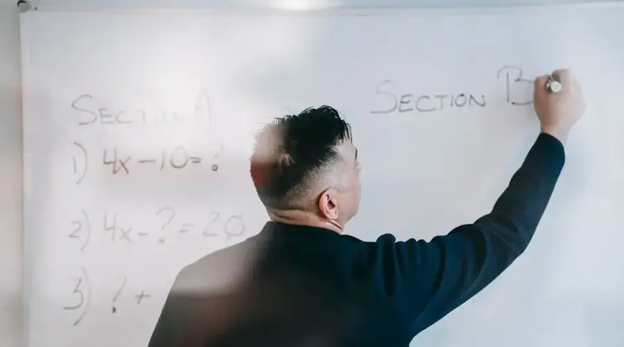 A male teacher writes equations on a whiteboard during a math lesson.