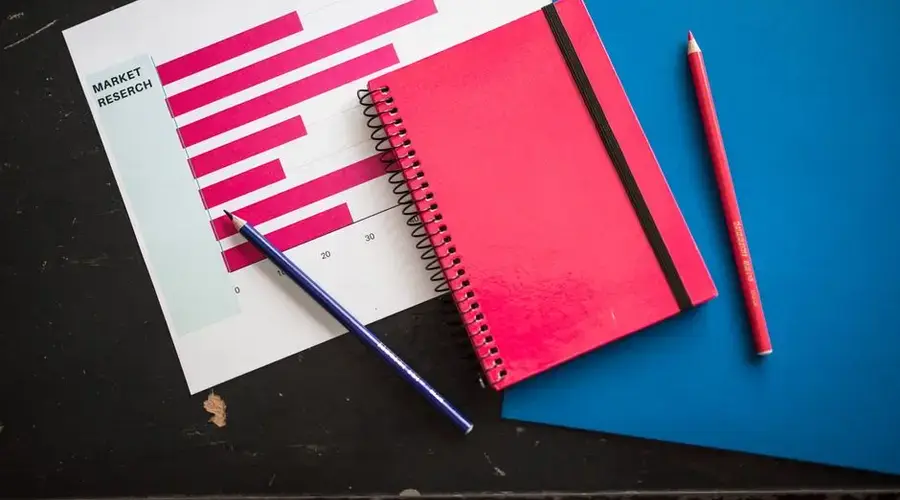 Overhead view of business chart with red notebook and colored pencils on table.