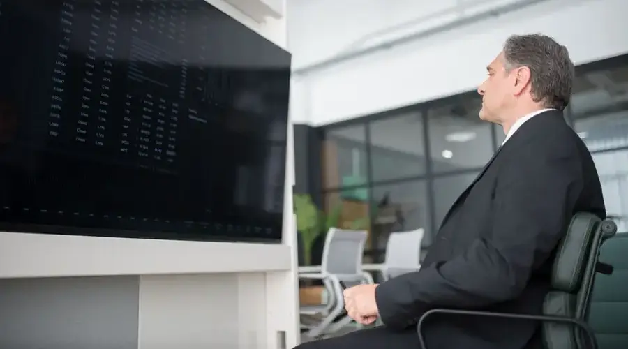 A professional businessman in a modern office analyzing stock market data on a large screen.