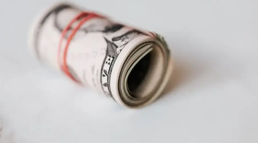 High angle roll of five dollar bills on white table tightened with red rubber band