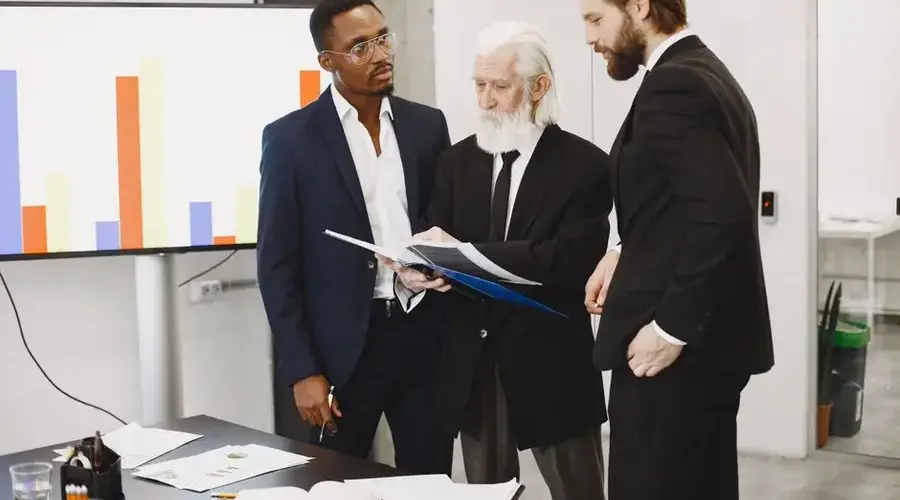 Three businessmen in suits discussing reports in a modern office setting.