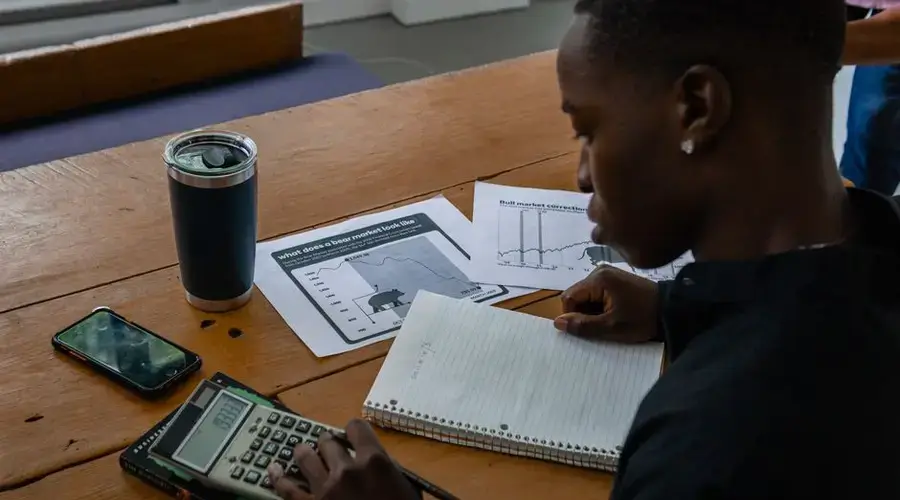Young professional evaluating financial data using a calculator and notes.