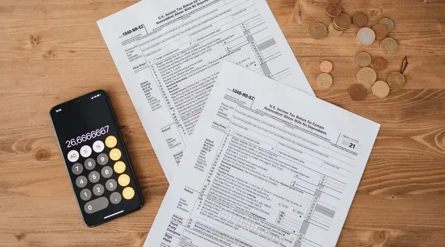 Top view of tax documents, calculator, and coins on wooden table.