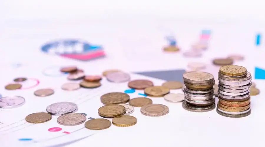 Stack of assorted coins with financial documents on a white background, highlighting the concept of savings.