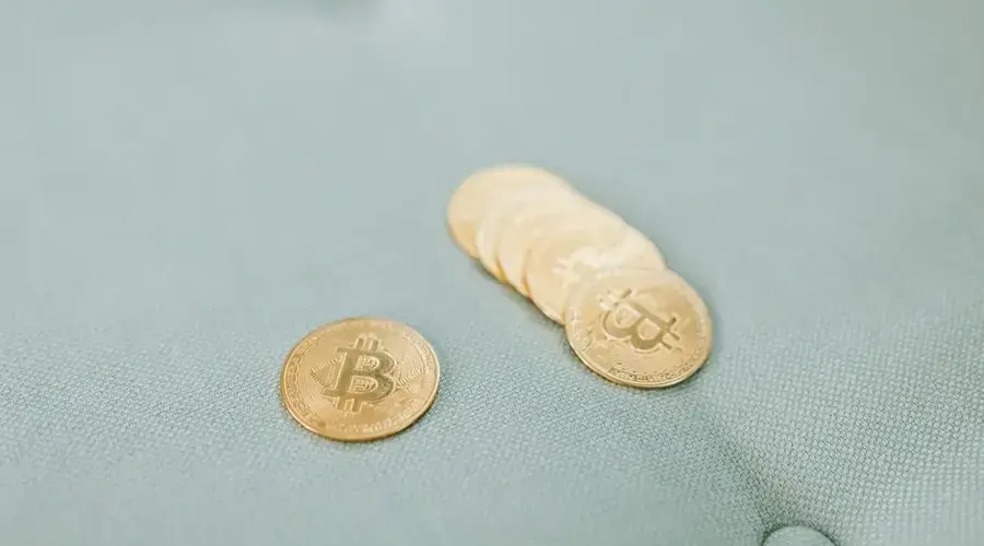 Close-up of gold Bitcoins laid on a soft blue fabric background, representing cryptocurrency wealth.