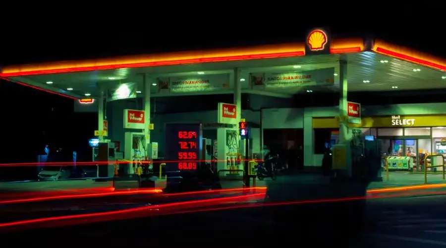 Illuminated Shell gas station with long exposure light trails at night.