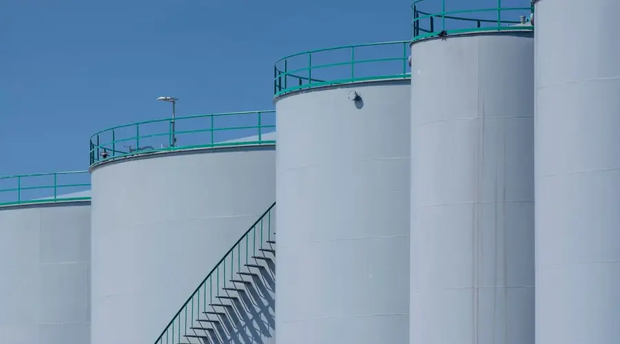 Large industrial storage tanks with green railings against a clear blue sky.