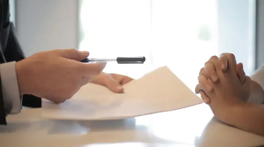 Side view of faceless formal man giving pen and paper to focused female with clenched hands at table on meeting