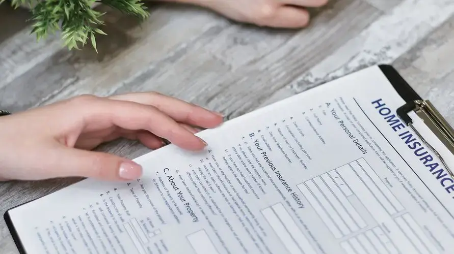 Close-up of hands holding a home insurance document indoors, showing personal details section.