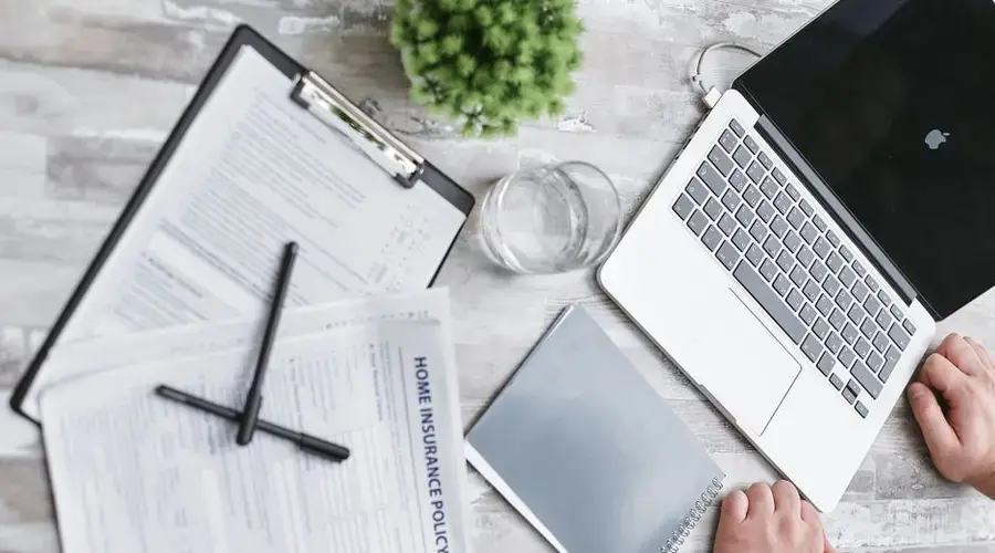 Top view of home insurance forms, laptop, and documents on a desk, conveying a professional office setting.