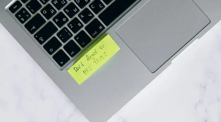 Close-up of a sticky note on a laptop reminding to pay taxes, emphasizing tax season.