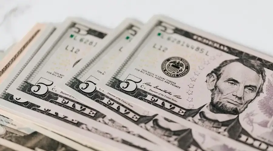 From above of pile of five dollar bills placed on white marble surface