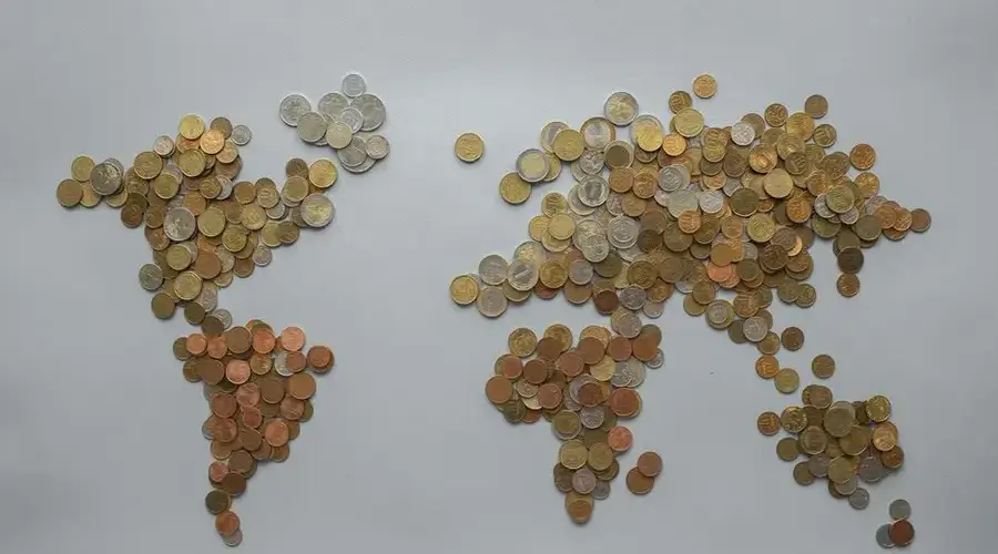 Creative world map made from assorted coins on a solid gray backdrop, symbolizing global finance.