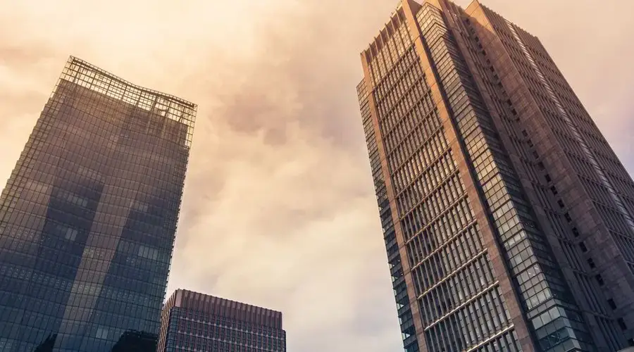 Modern skyscrapers in Tokyo with warm tones reflecting in glass against a cloudy sky.