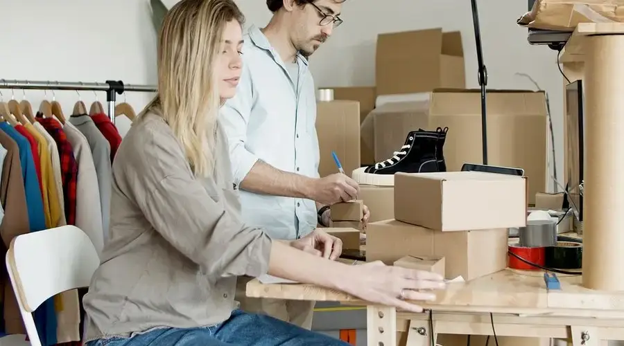 Business partners organizing inventory in an online store setup with clothes and boxes.