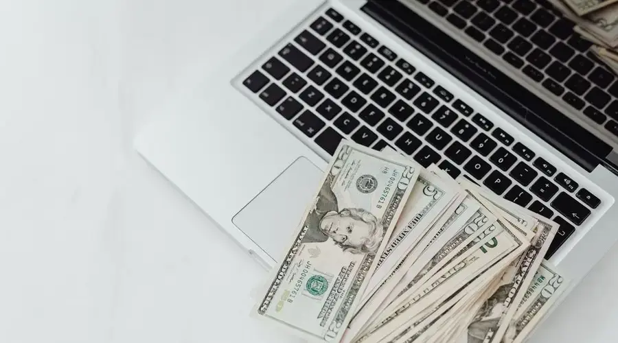 A stack of US dollar bills on a laptop keyboard representing online finance and budgeting.