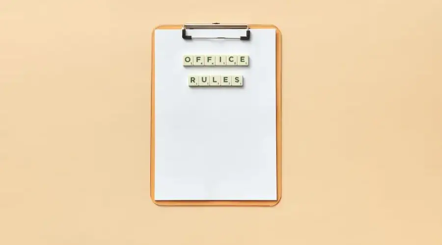 A clipboard with the phrase 'Office Rules' spelled out using Scrabble tiles on a beige background.