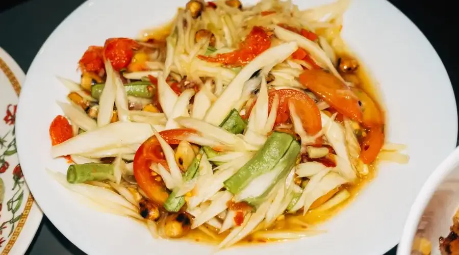 Close-up of a traditional Thai som tam papaya salad with fresh vegetables.