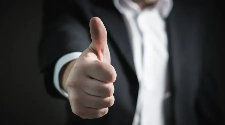 A close-up of a man's thumbs up gesture, symbolizing success and agreement.