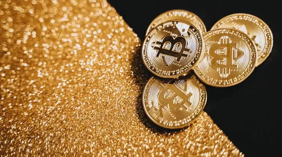 Gold Bitcoin coins displayed on a sparkling gold texture, representing digital currency and finance.