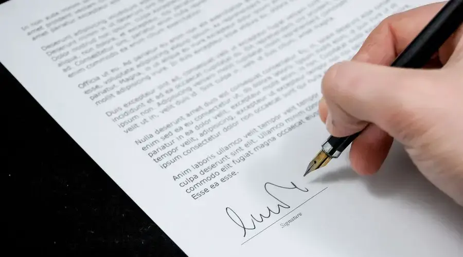 Close-up of a hand signing a formal document with a fountain pen, indicating agreement.