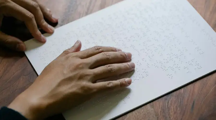 Hands gently read a Braille text sheet providing tactile learning experience.