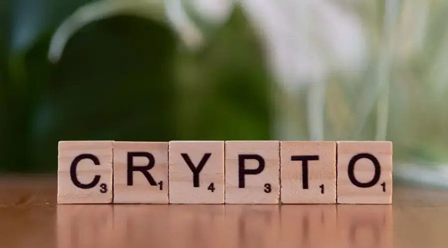 Wooden Scrabble tiles spelling 'CRYPTO' on a wooden surface with a blurred green background.