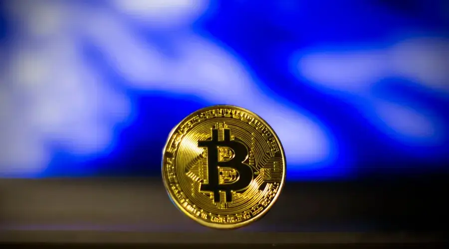 Close-up of a golden Bitcoin coin with a blurred blue abstract background, symbolizes digital currency.