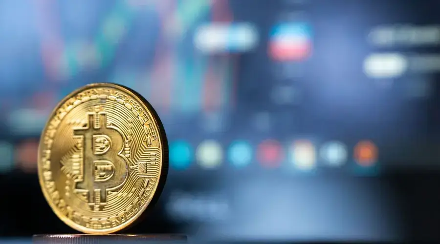 Gold Bitcoin coin with blurred financial chart in background, representing cryptocurrency trading.