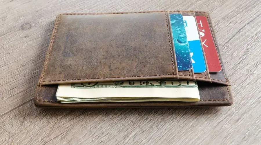 A brown leather wallet with cash and credit cards on a wooden surface.