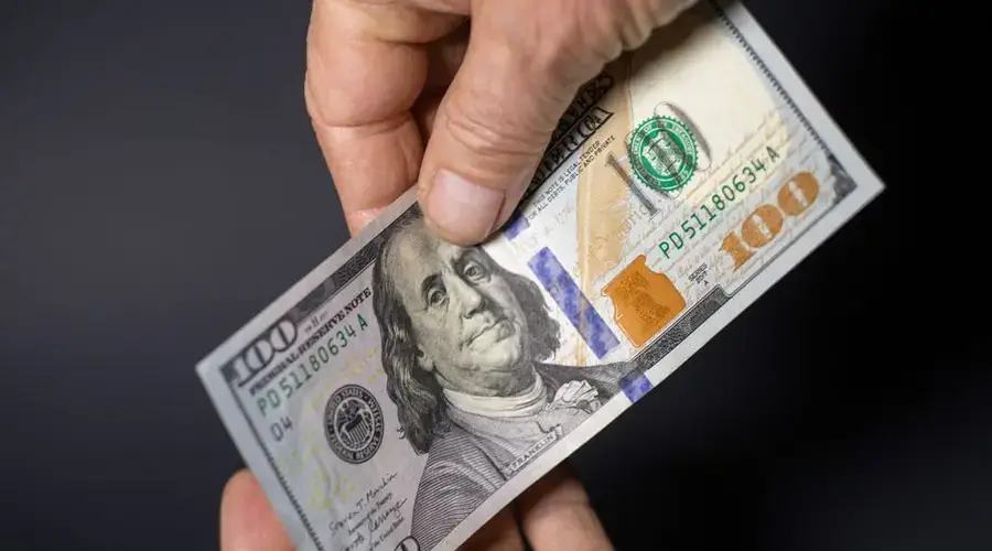 Detailed image of hands exchanging a crisp one hundred dollar bill, symbolizing financial transactions.