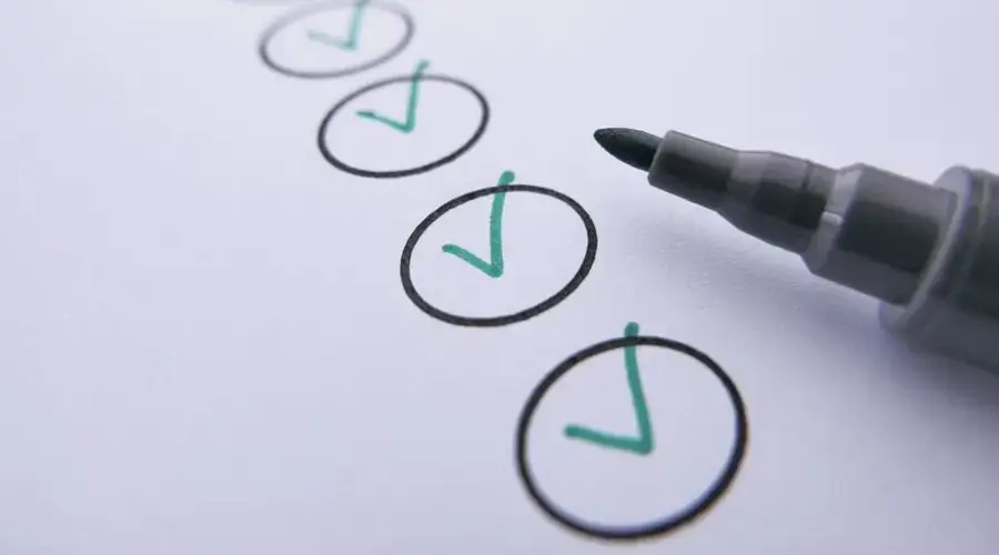 Close-up of a checklist with green checkmarks on white paper using a marker.