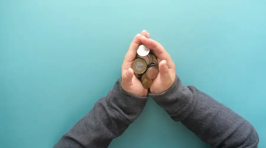 Two hands holding a stack of coins against a blue background, symbolizing savings or financial security.
