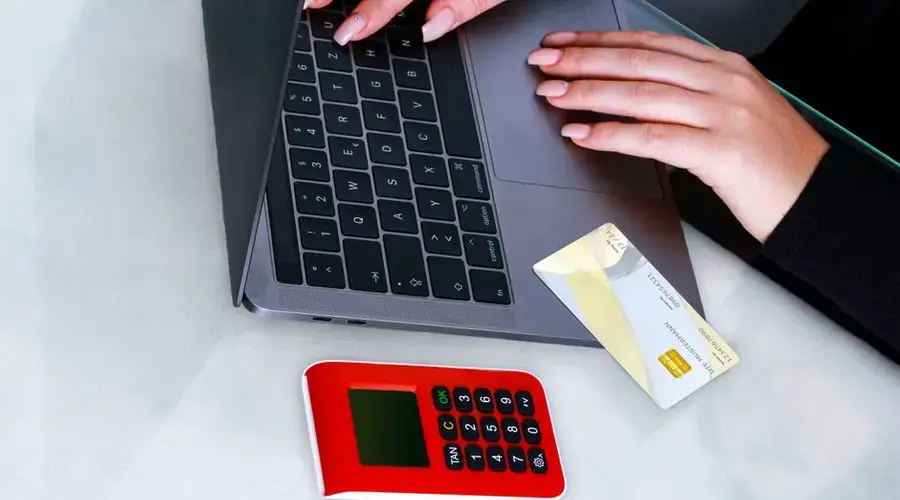 Hands using laptop with credit card and security device for online payment, emphasizing cybersecurity.