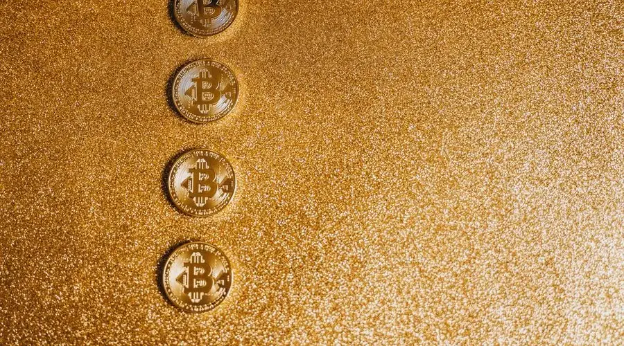 Four Bitcoin coins arranged on a shimmering gold glitter background with ample copyspace.