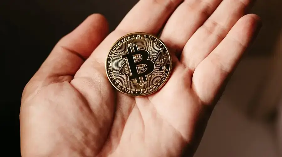 Close-up of a hand holding a Bitcoin coin, illustrating cryptocurrency concept.