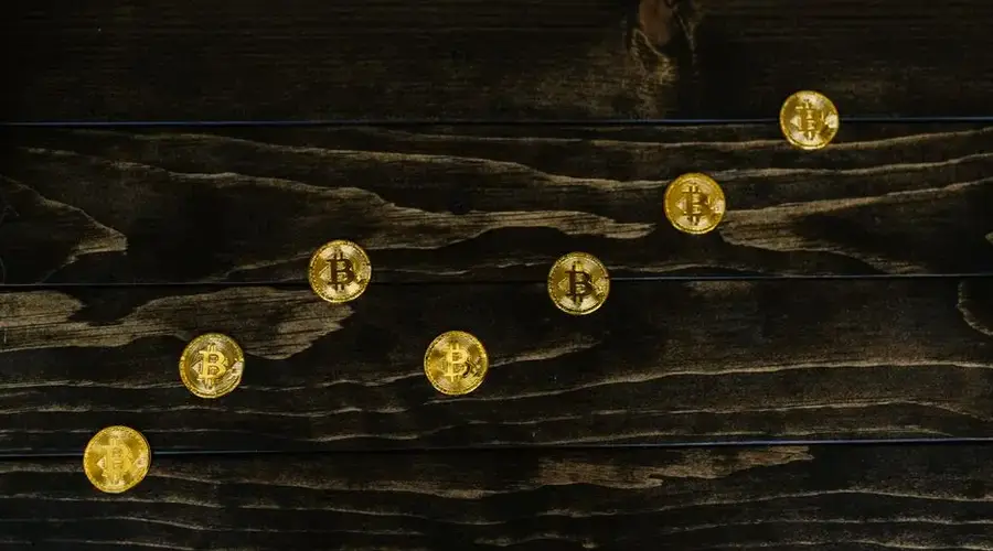 Gold-colored bitcoins arranged diagonally on a dark wooden surface.