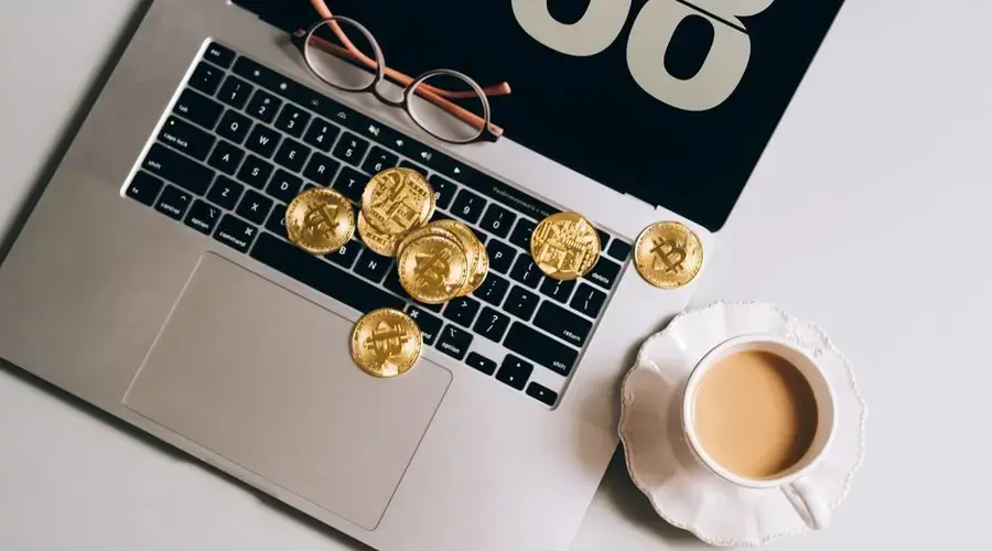 A laptop with bitcoin coins and a coffee mug, symbolizing cryptocurrency trading.
