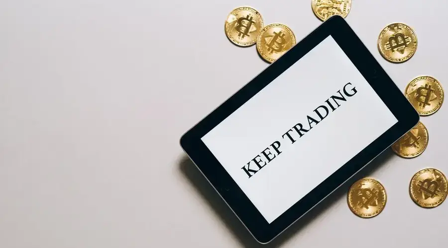 Tablet displaying 'Keep Trading' surrounded by Bitcoin coins on a white background, emphasizing digital currency and trading.