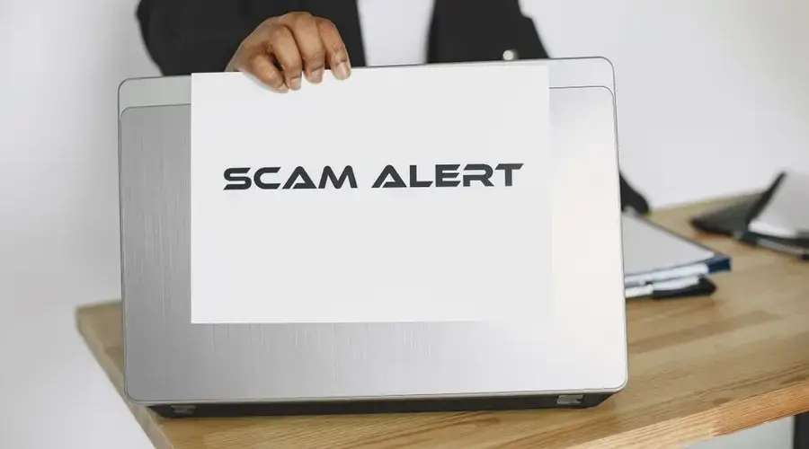 Business person holding a scam alert sign over a laptop, warning against online fraud.