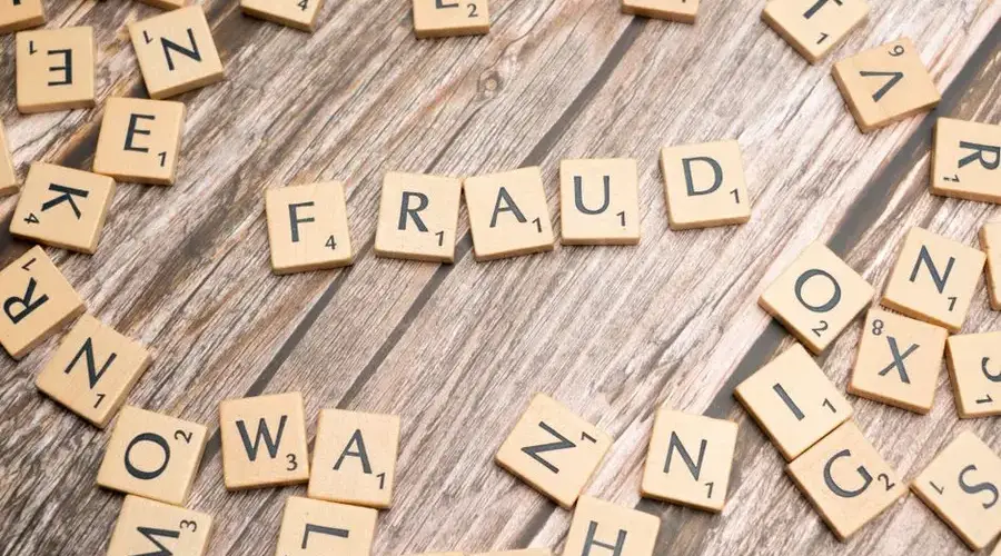 Alphabet tiles arranged to spell 'fraud' on a wooden surface, symbolizing deception.