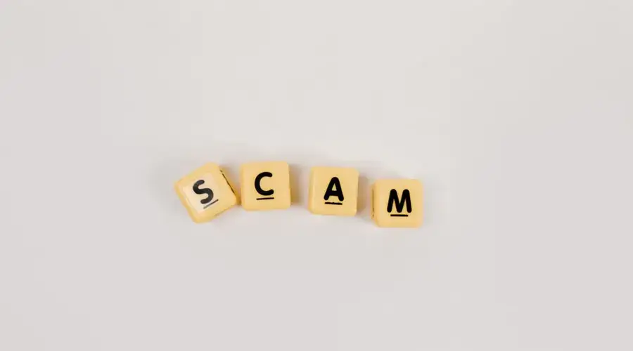 Four Scrabble tiles forming the word 'SCAM' on a neutral background, highlighting concepts like deceit.