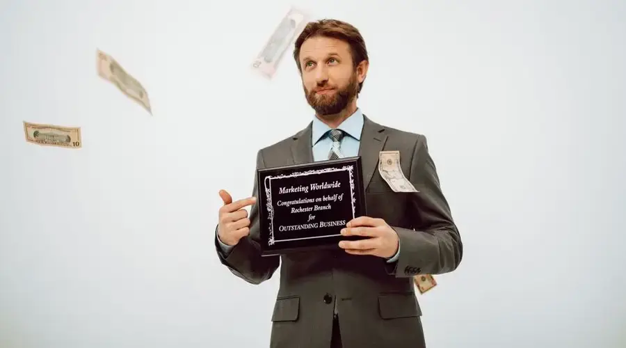 Businessman holding an award plaque, surrounded by falling cash, symbolizing success.