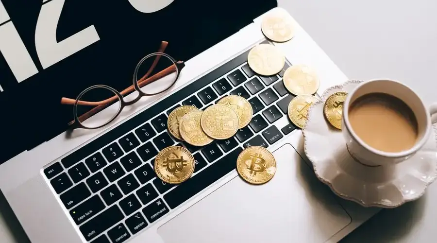 Laptop keyboard covered with Bitcoin coins and a coffee cup nearby, symbolizing cryptocurrency and work balance.