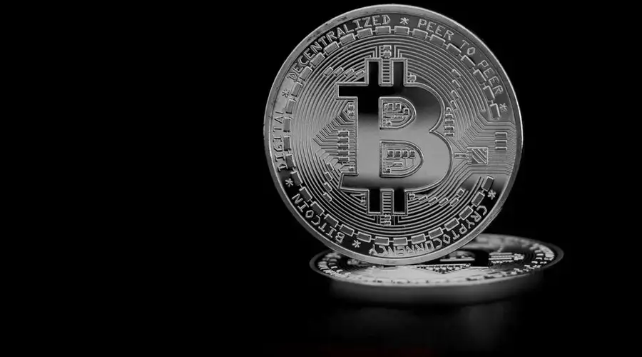 Close-up of a silver bitcoin coin, highlighting the cryptocurrency symbol on a black background.