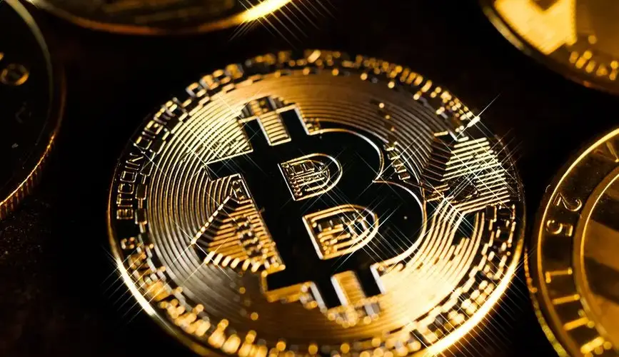 A detailed close-up shot of a shiny gold Bitcoin coin, highlighting the cryptocurrency symbol.