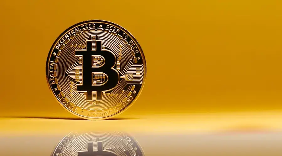 A shining Bitcoin coin placed on a reflective surface against a vibrant yellow background. Ideal for digital currency themes.