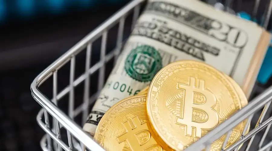Close-up of bitcoin coins and US dollar bills in a small shopping cart, symbolizing online shopping and cryptocurrency investment.