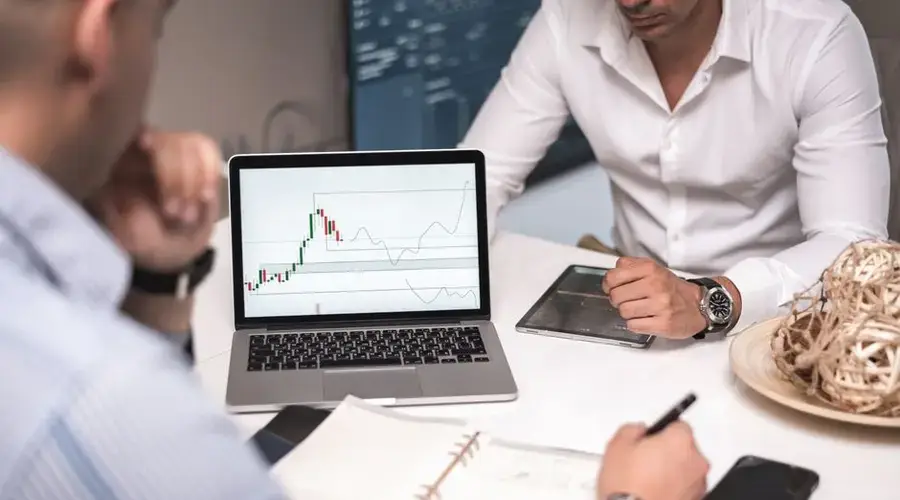 Team of professionals reviewing stock market charts and data on a laptop in a modern workspace.